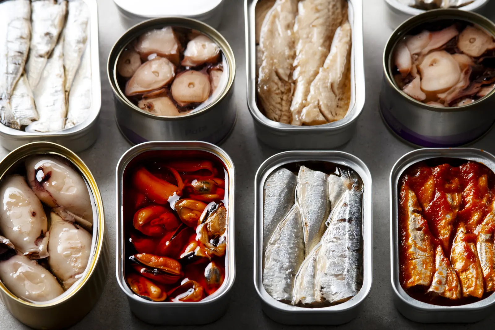 Latas de sardinas, mejillones, calamares y berberechos abiertas sobre metal